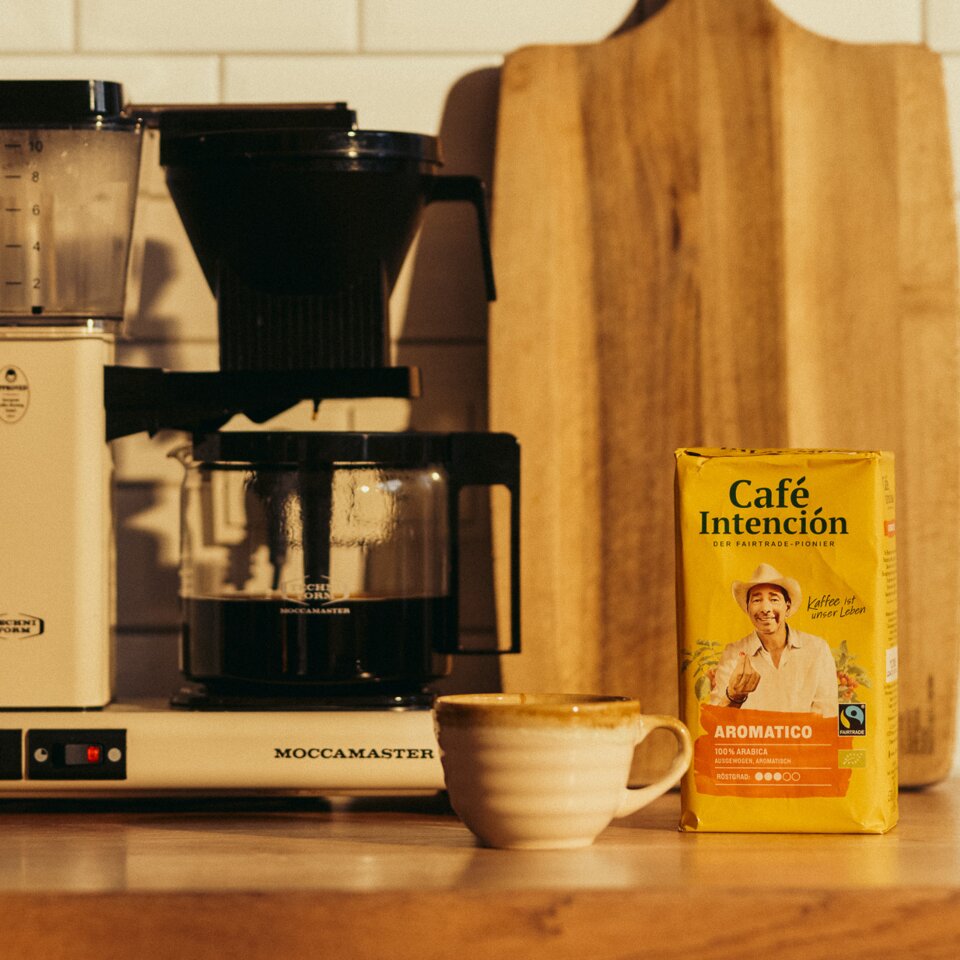 Eine Moccamaster-Kaffeemaschine neben einer Verpackung von „Café Intención“ und einer Tasse, in einer hellen Küchenumgebung.
